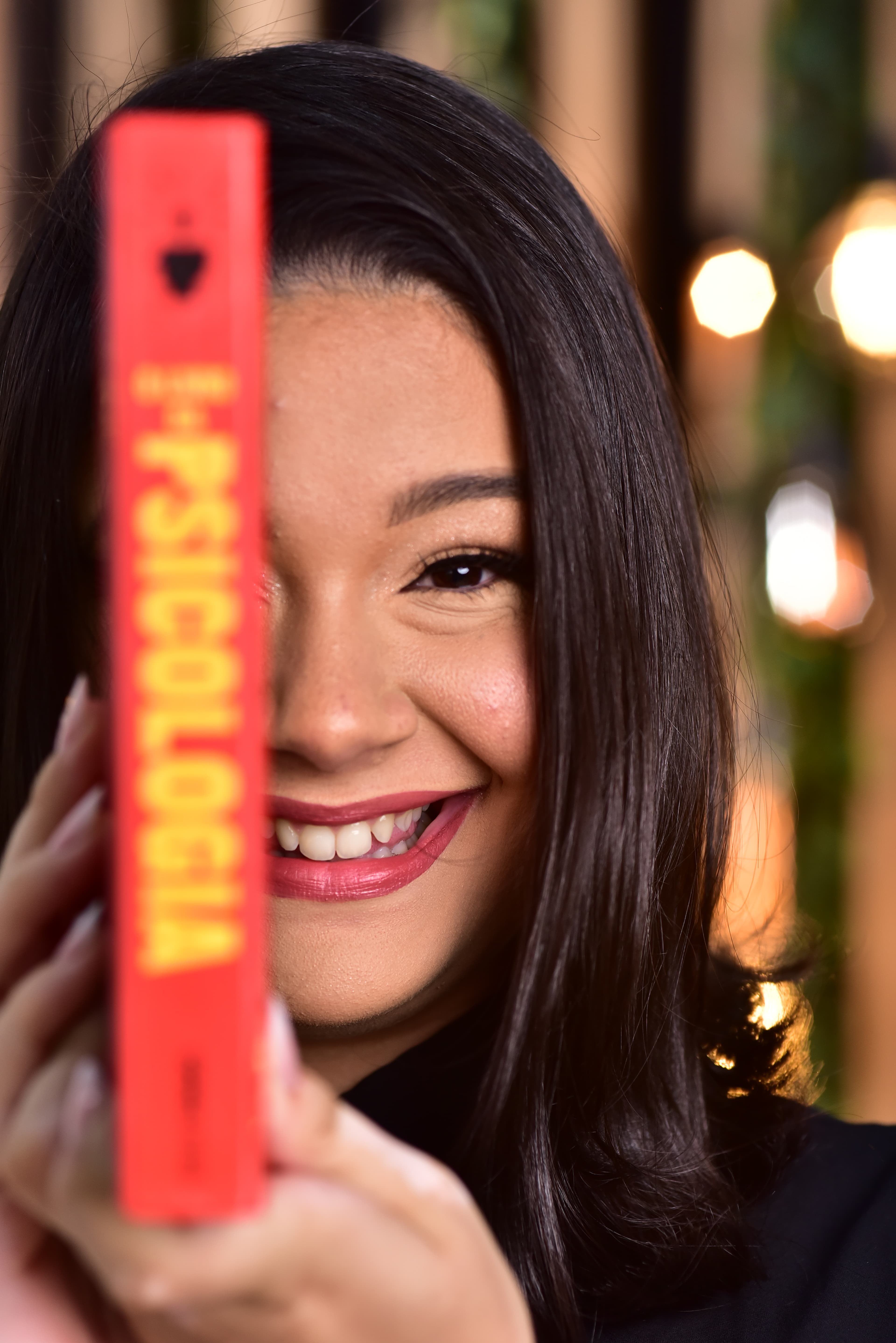 Psicóloga Bianca, com cabelo liso nos ombros, sorrindo e segurando um livro com o título 'Psicologia'