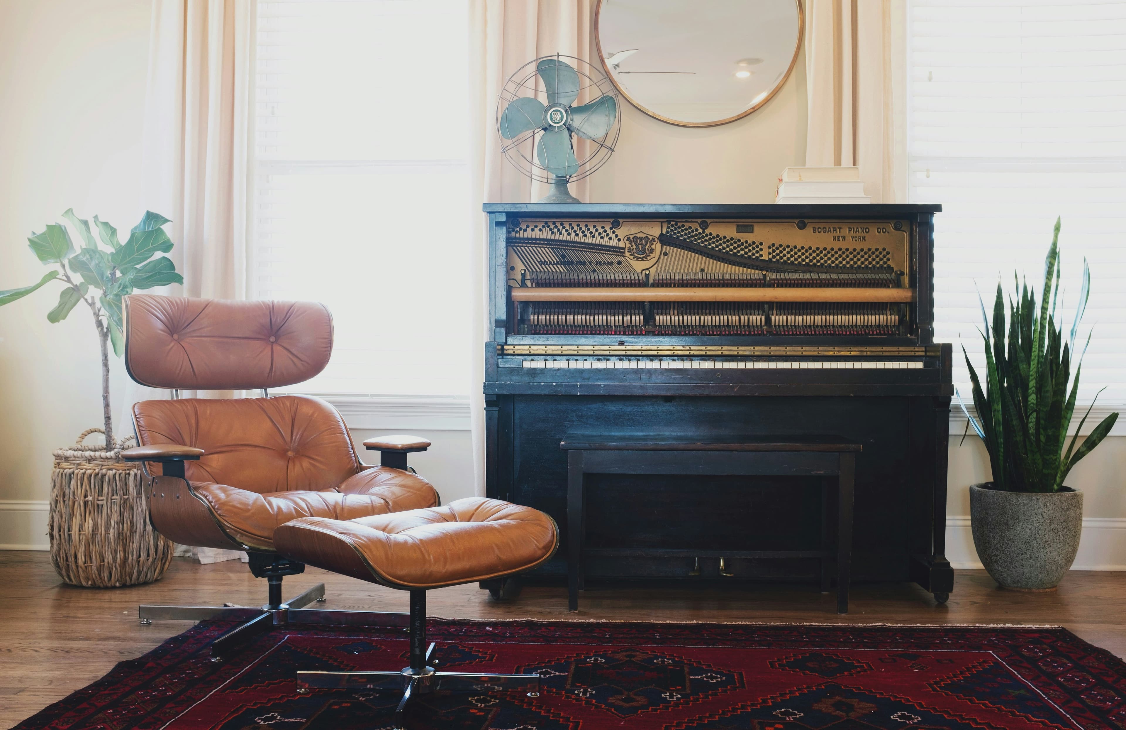 Sala aconchegante com uma poltrona marrom em primeiro plano, um piano e plantas ao fundo